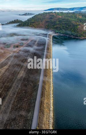 Vertikales Luftbild der Glenbawn Dam Mauer mit Morgennebel, der durch das umliegende Tal in NSW Australien driftet. Drohnenfotografie Stockfoto