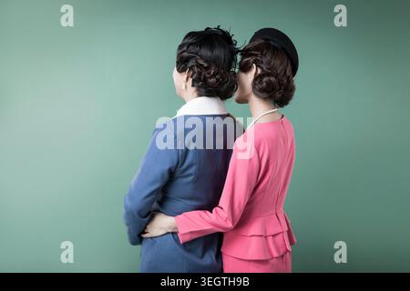 Zwei Frauen in Geschäftskleidung im Stil der 1960er Jahre teilen sich einen zärtlichen Moment in einer ruhigen, intimen Umgebung. Stockfoto