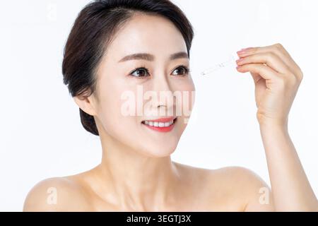 Eine Frau hält ein kleines Fläschchen mit Flüssigkeit und lächelt, ihre Augen und ihre Haut leuchten in einem subtilen, strahlenden Glanz. Stockfoto