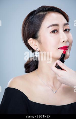 Eine Frau trägt Lippenstift in einem Studio-Setting auf. Stockfoto