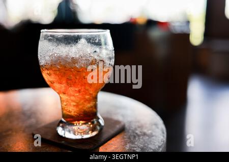Entspannendes kaltes Bernsteingetränk im Glas mit zerstoßenem Eis auf der Achterbahn über dem Tisch an der lokalen Bar bietet erfrischende Kälte und einladende Getränke für ein Erlebnis Stockfoto