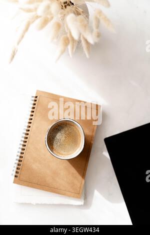 Minimaler Schreibtisch mit Kaffeetasse, Notebook- und Laptop-Ecke auf weißer Oberfläche, weichen Schatten und sauberer Arbeitsfläche. Draufsicht Stockfoto