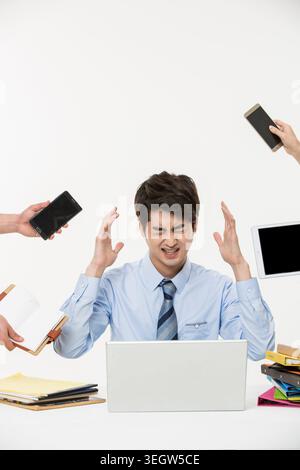 Ein gestresster Büromitarbeiter wird von mehreren Geräten und Aufgaben überfordert. Stockfoto