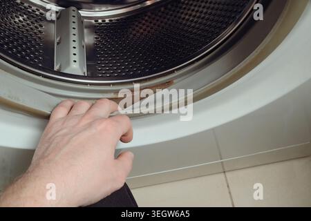 Verschmutztes, schimmeliges Dichtgummi der Waschmaschine. Die Person prüft den Schmutz auf dem Gummi einer Waschmaschine. Abgeschnittene Handwaschmaschine. Gummi Stockfoto