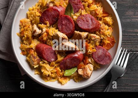 Traditionelles polnisches Bigos-Gericht oder Hunter's Stew mit Würstchen, Fleisch und Kohl in Keramikschüssel. Detaillierte Nahaufnahme. Geschmortes Sauerkraut mit Bratwurst. Stockfoto