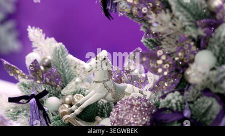 Schaukelpferdeschmuck, der den Weihnachtsbaum mit lila Pailletten, Glitzer und Bändern dekoriert, schafft eine festliche Atmosphäre Stockfoto