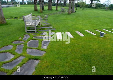 Ein Steinweg führt durch einen üppig grünen Park, umgeben von Palmen und Bänken, unter einem sonnigen Himmel. Stockfoto