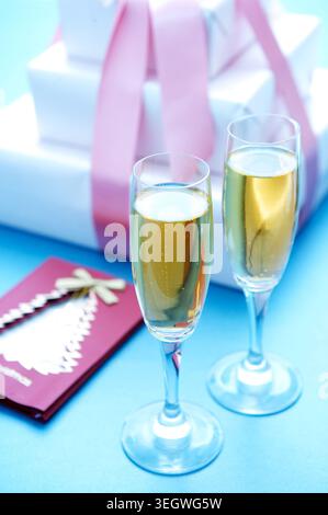 Zwei Sektgläser sitzen auf einem blauen Tisch neben einem Stapel weißer Geschenkboxen und einer roten Karte. Stockfoto