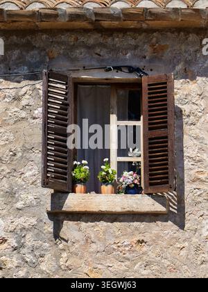 Offene Holzläden mit Blumen an einer Steinfassade auf Mallorca, sonnige mediterrane Wohnszene. Stockfoto