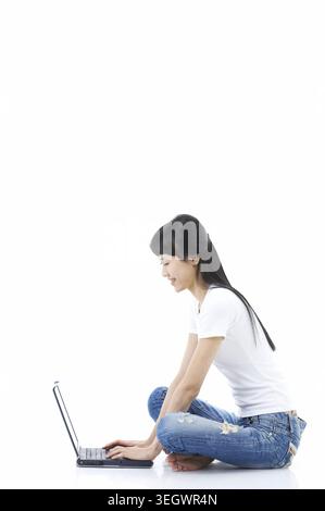 Eine junge Frau sitzt auf dem Boden und arbeitet an ihrem Laptop. Stockfoto