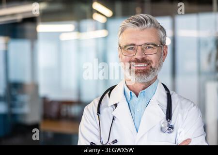 Ein reifer Arzt mit verschreibungspflichtiger Brille und weißem Mantel mit Stethoskop lächelt zuversichtlich und zeigt Expertise und Vertrauen in ein modernes Heil Stockfoto