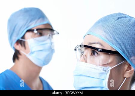 Chirurgen in chirurgischen Masken und Schutzbrillen stehen in einem Krankenhausflur und warten auf die Ankunft eines Patienten. Stockfoto