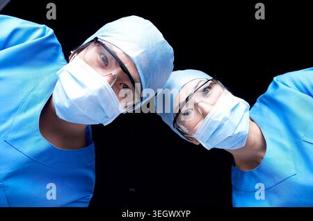 Zwei Chirurgen in chirurgischer Kleidung schauen von einem OP-Tisch aus in die Kamera. Stockfoto