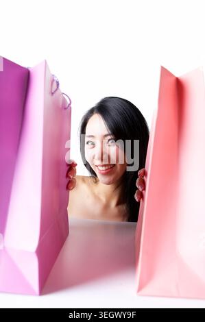 Eine Frau schaut hinter zwei großen Einkaufstaschen heraus und lächelt. Stockfoto
