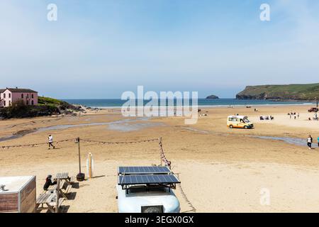 Die Strandszene in Polzeath in Cornwall zeigt eine breite Sandküste, bei der die Menschen das sonnige Wetter genießen. Kleine Strandstrukturen, einschließlich eines Trails Stockfoto