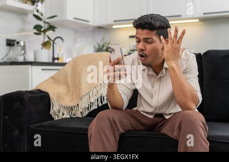 Der indische Mann zu Hause spielt die mobile Spielrunde verliert die Facepalm verärgert und ist bereit für das Rückspiel. Arabian Guy auf Sofa Tips versuchen Sie es erneut auf Smartphone Pläne Comeback konzentriert sich auf die nächste Stufe und die Wiederherstellung der Punktzahl Stockfoto