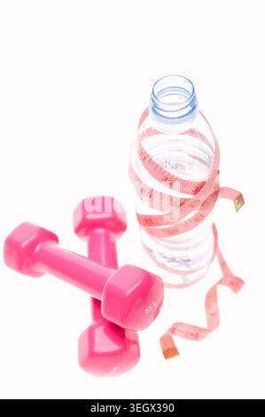 Eine Wasserflasche ist von einem Maßband und einem Paar rosafarbenen Kurzhanteln auf weißem Hintergrund umgeben. Stockfoto