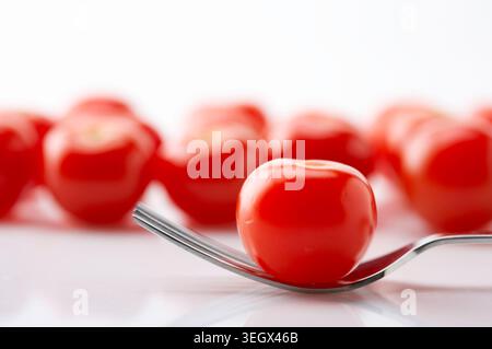 Eine einzelne, reife Tomate wird auf die Spitze einer Gabel gelegt, die auf einer weißen Oberfläche aufliegt. Stockfoto
