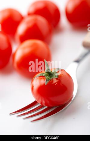 Eine einzelne, reife Tomate wird vorsichtig auf die Spitze einer Gabel gelegt, die zum Verzehr bereit ist. Stockfoto
