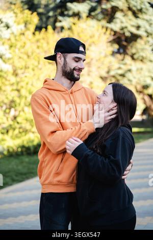 Junge kaukasische Paare zeigen Zuneigung und emotionale Verbundenheit im Freien, während sie zusammen in einem sonnigen Park stehen. Liebe Partnerschaft und Elternschaft li Stockfoto