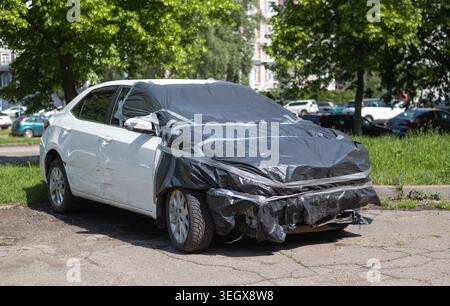 Beschädigte weiße Limousine mit schwarzem Plastik und Klebeband, die nach einem Unfall auf der Straße geparkt wurde. Stockfoto