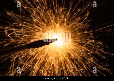 Makroaufnahme von hellen goldenen Funken, die von einem brennenden Funken oder Pyrotechnik auf schwarzem Hintergrund fliegen Stockfoto