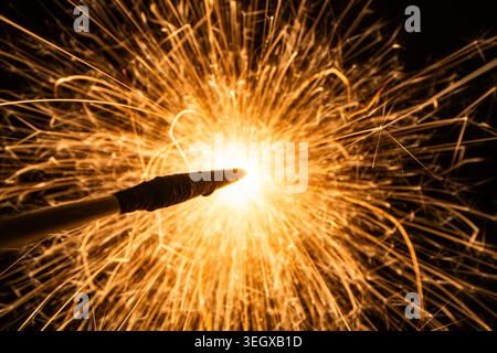 Makroaufnahme von hellen goldenen Funken, die von einem brennenden Funken oder Pyrotechnik auf schwarzem Hintergrund fliegen Stockfoto