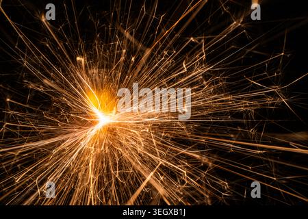 Makroaufnahme von hellen goldenen Funken, die von einem brennenden Funken oder Pyrotechnik auf schwarzem Hintergrund fliegen Stockfoto