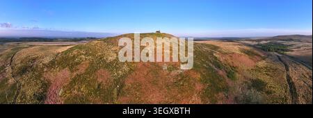 Blick aus der Vogelperspektive auf die Chapelle Saint Michel de Brasparts auf einem Hügel, umgeben von einer weiten Moorlandschaft und Heide unter einem klaren blauen Himmel Saint-Rivoal, Bretagne Stockfoto