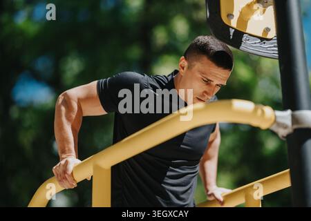 Fitter Mann, der während eines sonnigen Workouts Trizeps auf gelben DIP-Bars im Freien macht Stockfoto