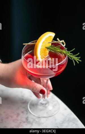 Erfrischender Cocktail garniert mit Orange und Rosmarin in einem eleganten Glas auf einem Marmortisch Stockfoto