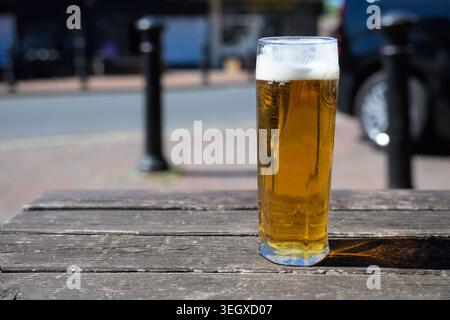 Erfrischendes Bier auf einer Pub-Bank im Freien bei strahlendem Sonnenschein mit klarem blauem Himmel, ideal für Sommerurlaub und Pub-Lifestyle-Themen. Stockfoto