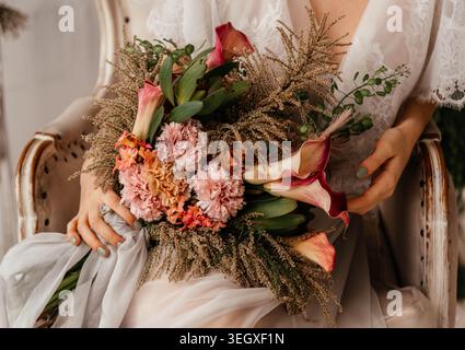 Ein Mädchen hält einen schönen Blumenstrauß in den Händen. Brautstrauß. Nelken, Calla-Lilien, getrocknete Blüten werden in einer Komposition gesammelt. Stockfoto