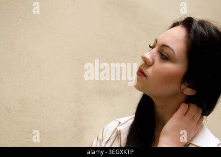 Nahaufnahme-Porträt einer jungen Frau, die ihr Haar neben einer schlichten neutralen Wand berührt, mit Kopierplatz Stockfoto