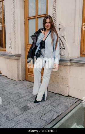 Frau Mode Stil junge Frau trägt Jeans und ein leichtes Hemd, das sich an der Steinfassade in der Stadtstraße anlehnt Stockfoto