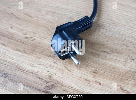 Schwarzer Kunststoff-Netzstecker mit Metallstiften, die auf einem Holztisch getrennt liegen. Gerätekabel vor dem Einstecken der Steckdose abgenommen. Energiesparen Stockfoto