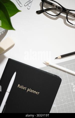 Flacher Arbeitsbereich mit Planer, Brillen, Bleistiften und Bürobedarf auf weißem Schreibtisch. Kopierbereich. Stockfoto