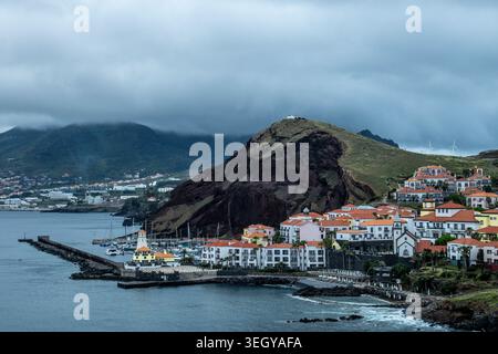 Eine wunderschöne, stimmungsvolle Landschaft, die einen malerischen Yachthafen und Küstenstadt auf einer Vulkaninsel, wahrscheinlich Madeira (Quinta do Lorde), erfasst. Das Bild f Stockfoto