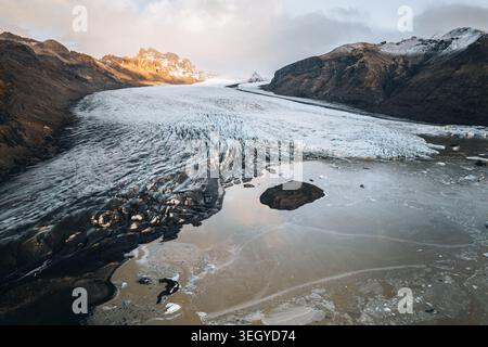 Aus der Vogelperspektive auf den Skaftafell-Gletscher mit seiner rissigen Eisoberfläche und zerklüfteten Berggipfeln bei weichem Sonnenuntergang, Skaftafell, Sveitarfelagid Horna Stockfoto
