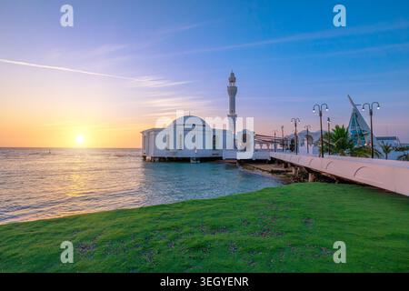 Bei Sonnenuntergang geht die Sonne auf der Al Rahmah Moschee an der Jeddah Waterfront mit dem JYC Jeddah Yacht Club Gebäude an der Roten Küste Saudi-Arabiens unter Stockfoto