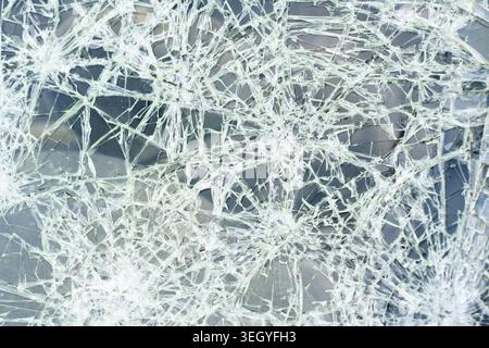 Nahaufnahme eines völlig zertrümmerten und zertrümmerten Fahrzeugglasfensters mit Spinnennetz-Rissstruktur im Hintergrund. Stockfoto