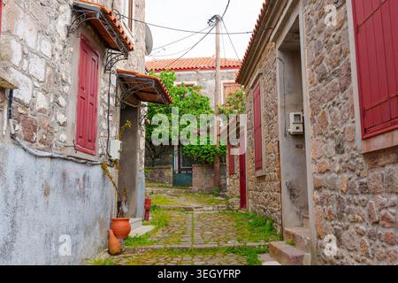 Enge Kopfsteinpflasterallee, die sich zwischen traditionellen rustikalen Steinhäusern mit roten Holzläden im historischen Dorf Molyvos, Lesbos, Greec schlängelt Stockfoto