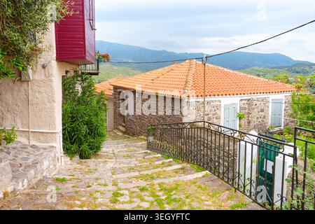 Kopfsteinpflasterallee führt vorbei an traditionellen Steinhäusern mit Terrakotta-Ziegeldächern im historischen Dorf Molyvos auf der Insel Lesbos, Griechenland, unter einem Stockfoto