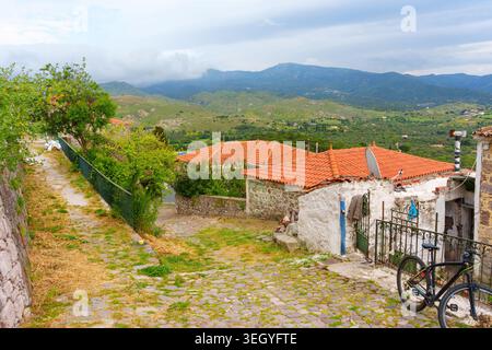 Kopfsteinpflasterallee schlängelt sich vorbei an traditionellen Steinhäusern mit roten Ziegeldächern im malerischen Dorf Molyvos auf der Insel Lesbos, Griechenland, mit Berg l Stockfoto