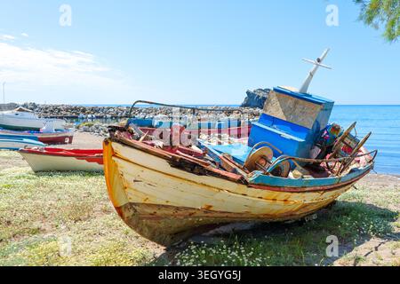 Alte hölzerne Fischerboote mit abblätternder Farbe ruhen an den Sandstränden von Skala Eresou, Lesbos, Griechenland, unter einem klaren blauen Himmel und mit wunderschönen Mariti Stockfoto