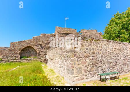 Die alten Steinbefestigungen der Burg Molyvos stehen hoch vor einem klaren blauen Himmel auf der Insel Lesbos, mit einer griechischen Flagge, die auf dem zerklüfteten Byz winkt Stockfoto
