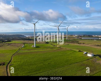Luftaufnahme von Windturbinen, die auf grünen Feldern in der Nähe der Küste unter einem bewölkten Himmel in Portugal stehen. Stockfoto