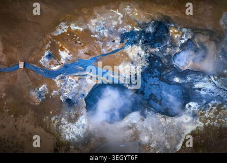Aus der Vogelperspektive auf ein geothermisches Feld mit leuchtenden blauen Schlammbecken, aufsteigenden Dampfdüsen und mineralreicher orangener Erde in der Vulkanlandschaft von Stockfoto
