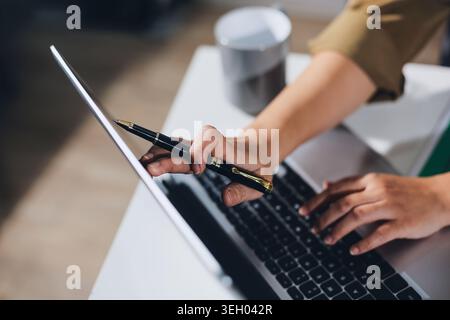 Junge asiatische Frau, die spät an ihrem Schreibtisch arbeitet, einen Videoanruf oder ein Online-Meeting mit einem Laptop führt, Daten analysiert und Geschäftsfinanzen in einem verwaltet Stockfoto