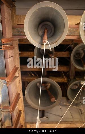 Seile hängen an mehreren großen Glocken in einem Glockenturm. Die Struktur zeigt Holzbalken und das Design für das Klingeln der Glocken. Sonnenlicht illumina Stockfoto